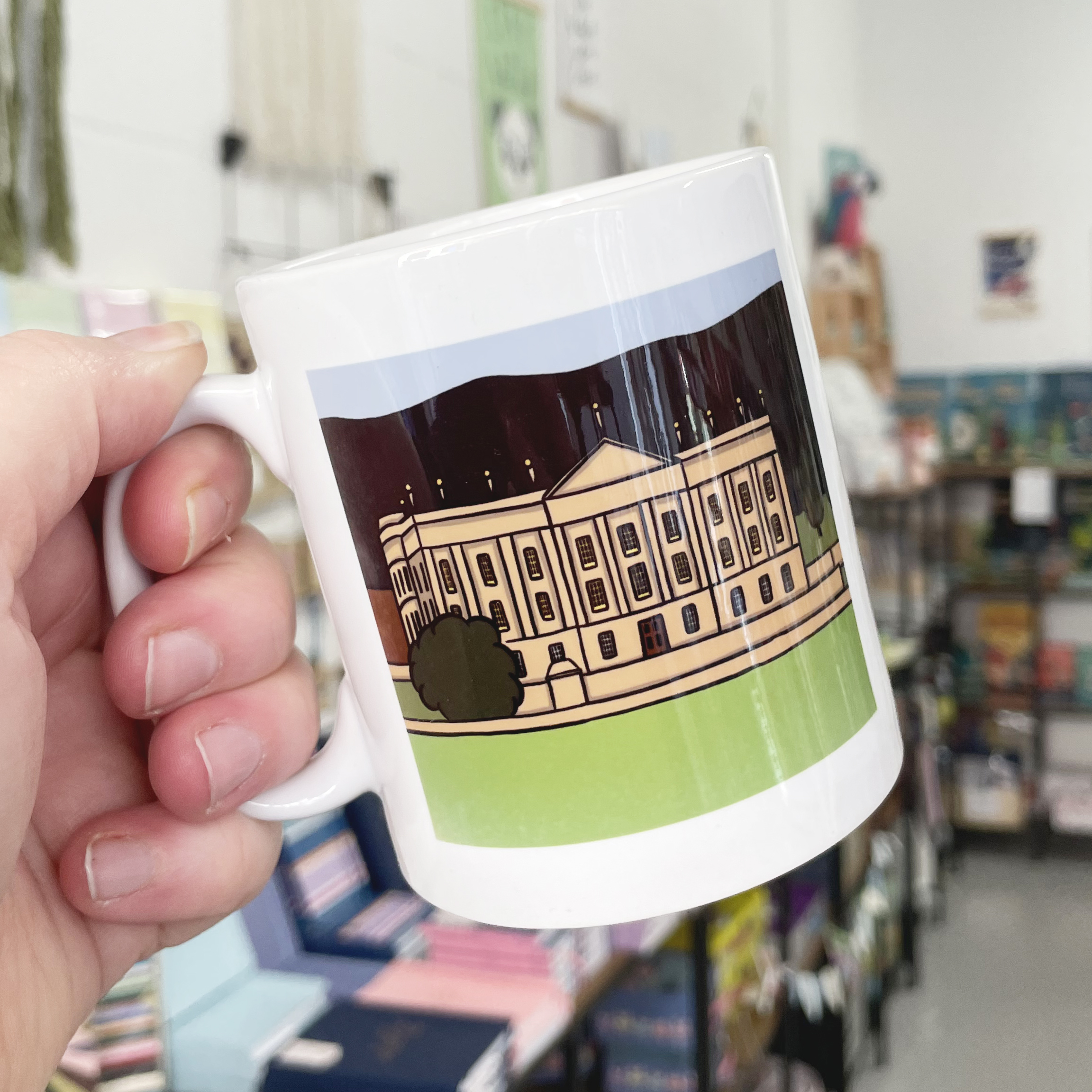 An illustration of Chatsworth House printed onto a white mug. The mug is being held by the handle.